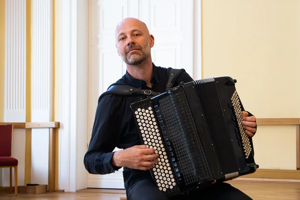 Harald Oeler mit Akkordeon im hellen Musikraum mit Paneeltüren